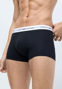 Sorte bomulds boxer shorts med en hvid elastisk talje, der har "TOMMY HILFIGER" logo. Designet er tætsiddende med en glat finish.