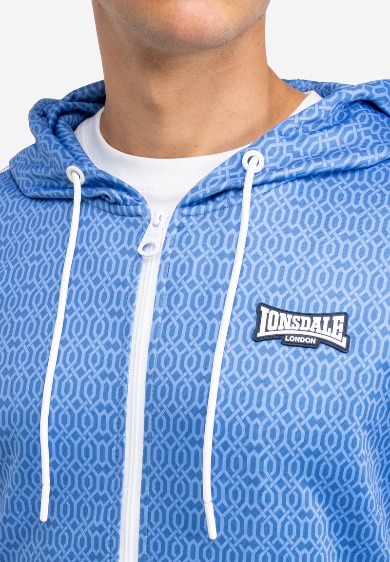 Blaues Zip-Hoodie mit geometrischem Muster, weißen Kordeln und einem Lonsdale London Logo-Patch auf der Brust. Glatte Stoffstruktur.