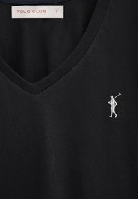 Chemise noire à col en V avec petit joueur de polo brodé en blanc sur le côté droit de la poitrine et étiquette "POLO CLUB" à l'intérieur de l'encolure.