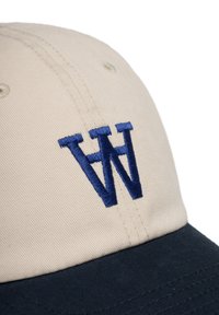 Beige baseball cap with a navy curved visor. Features a large embroidered "W" in dark blue on the front. Made of cotton, with ventilation holes.