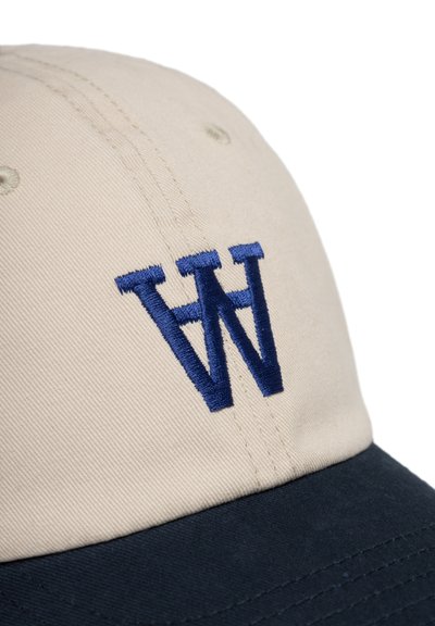 Casquette de baseball beige avec un visière courbée bleu marine. Présente un grand "W" brodé en bleu foncé à l'avant. Fabriquée en coton, avec des trous de ventilation.