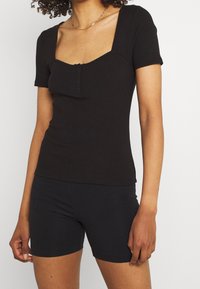 Svart ribbad kortärmad topp med fyrkantig halsringning och placket med tre knappar. Figursydd design i kombination med svarta shorts. Mjuk tygtextur.