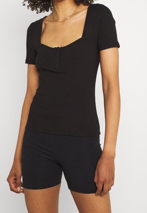 Schwarzes geripptes Kurzarmoberteil mit quadratischem Ausschnitt und einem dreiknöpfigen Schlitz. Figurbetontes Design kombiniert mit schwarzen Shorts. Weicher Stoff.