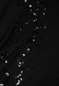 Schwarzer Stoff mit glatter Textur, der mit verstreuten schwarzen und silbernen Pailletten in einem dekorativen Muster verziert ist.