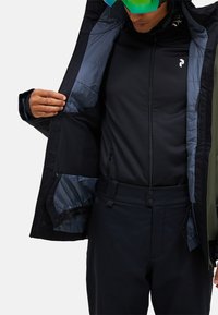 Skijacke mit schwarzer Außenseite und hellblauer Innenfütterung, ausgestattet mit mehreren Taschen und durchgehendem Reißverschluss, getragen über einer schwarzen Zwischenschicht und Hose.