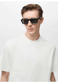 Ochelari de soare negri, rectangulari, cu lentile întunecate, purtați împreună cu un tricou simplu de culoare deschisă, cu decolteu rotund. Texturi netede vizibile.