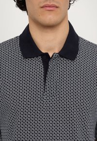Mørkeblå polo skjorte med et geometrisk hvitt mønster, med en mørk krage og to-knappers placket, laget av glattet stoff.