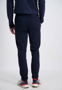 Marineblaues Slim-Fit-Hosenmodell, ausgestattet mit Gesäßtaschen und einer glatten Textur, kombiniert mit weißen und roten Sneakern mit blauen Akzenten.