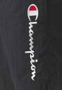Námornícke šortky vyrobené z ľahkého materiálu, s bielym vyšitým textom "Champion" a červenobielym logom nad ním.