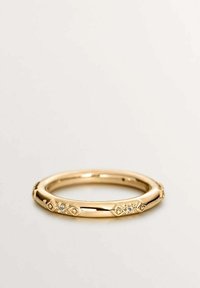 Anillo dorado con patrones geométricos y pequeñas piedras preciosas transparentes. Textura suave y pulida con forma redondeada.