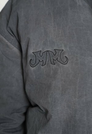 Chaqueta gris con acabado texturizado, que presenta un logo bordado en un gris más oscuro en el lado izquierdo. El material parece duradero y resistente.
