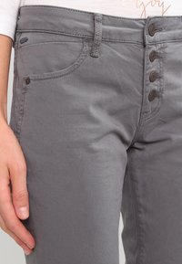 Pantalones de mezcla de algodón gris con cierre de cinco botones, dos bolsillos delanteros y tejido texturizado con sutiles líneas diagonales.