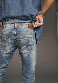 Lichtblauwe denim jeans met een iets vervaagde uitstraling, voorzien van twee achterzakken en een leren patch in bruin op de tailleband.