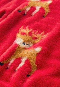 Red fabric with a soft, fuzzy texture featuring reindeer motifs in brown and white, accented with black dots and gold crowns.