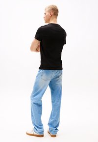 Tricou negru cu mânecă scurtă, asortat cu blugi drepți de culoare albastru deschis și adidași albi. Ținuta are un croi casual, relaxat.