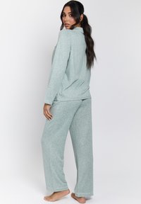 Conjunto de pijama de color verde claro y textura, que incluye una parte superior de mangas largas y pantalones holgados. La tela presenta un patrón sutil y cuenta con puños en los tobillos.