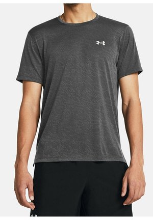 Mężczyzna w ciemnoszarej sportowej koszulce z krótkim rękawem i subtelnym wzorem, z małym białym logo Under Armour na piersi, w połączeniu z czarnymi spodenkami.