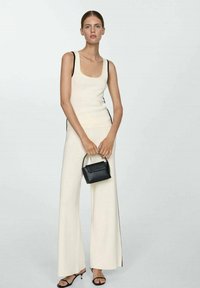 Cream-colored tank top and wide-leg pants with black side accents. Model holding a small black textured handbag, wearing black heeled sandals.