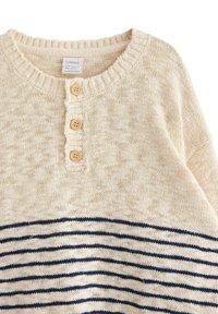 Strikket beige sweater med et ribbet halsudskærning, tre træknapper og marineblå stribede detaljer på den nederste halvdel. Blød tekstur.
