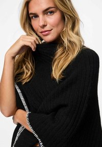 Poncho nero lavorato a maglia con colletto alto, con bordo in contrasto di filo bianco lungo i bordi e tessuto testurizzato.