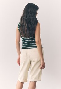 Débardeur à rayures vertes associé à un pantalon capri couleur crème. Le tissu est lisse ; le pantalon est doté de revers roulés et de poches arrière.