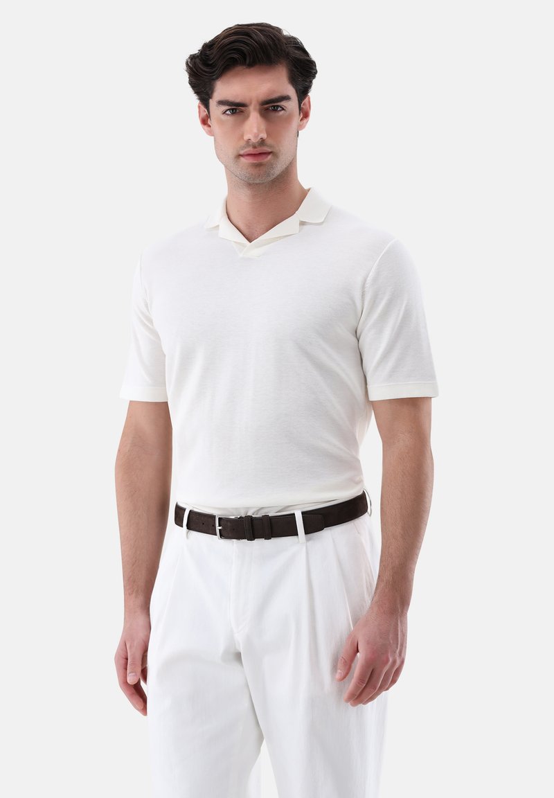 Weißes Poloshirt mit V-Ausschnitt, kurzen Ärmeln und strukturiertem Stoff, kombiniert mit weißen Hosen und einem braunen Leder-Gürtel.