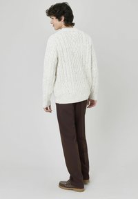 Pull en laine torsadée épais avec un col rond et un ourlet côtelé, associé à un pantalon marron et des chaussures marron clair. Vue arrière.