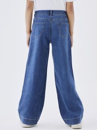 Breda ben, hög midja denimjeans i medelblått med en slät yta, två bakfickor och uppvikta fållar, tillsammans med en enkel vit topp.