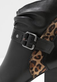 Musta nilkkaboot, jossa on kiiltävää nahkaa, teksturoitu leopardikuosisivu ja hopeinen solkihima. Tukeva korko.