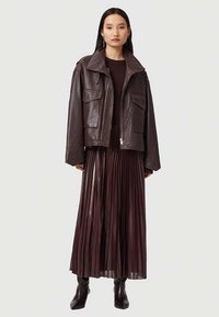 Ruda odinė striukė su plačiu apykakliu, dviem priekinių kišenių, derinama su ilga raukšlėta slyvų spalvos suknele ir auliniais batais.