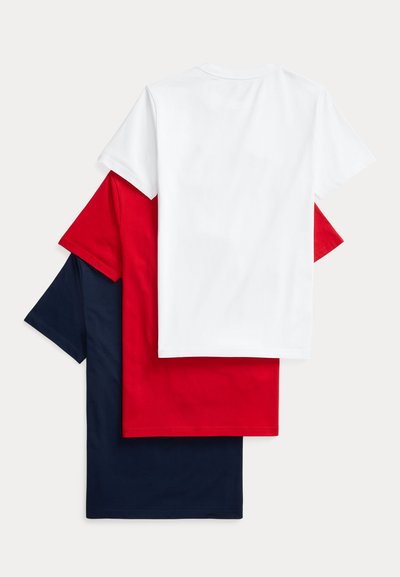 Στοίβα από τρία μονόχρωμα κοντομάνικα t-shirts με στρογγυλή λαιμόκοψη σε λευκό, κόκκινο και σκούρο μπλε, τοποθετημένα επικαλυπτόμενα σε ανοιχτό φόντο.