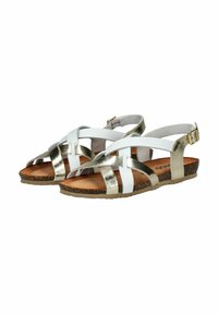 Sandalias de tiras con parte superior sintética blanca y acentos metálicos dorados. Planas, con una suela texturizada marrón y correa ajustable en el tobillo.