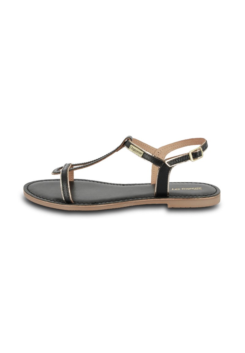 Sandale T-strap en cuir noir avec une semelle intérieure marron clair, une bride de cheville réglable et un détail de marque en ton doré. Design à semelle plate.