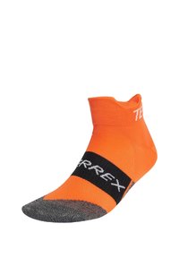 Calcetín atlético naranja con diseño de corte bajo, cuerpo de punto texturizado, y una banda negra con el texto blanco "TERREX" en la parte media del pie. Detalle gris en la punta.