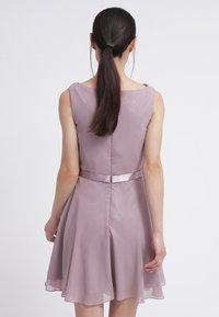 Sirôtková šifónová šaty s rozšířenou sukní, bezrukávovým střihem a saténovým páskem detailu v pase. Hladká textura s volným siluetou.