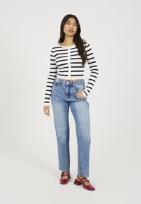 Pasiasty, prążkowany, krótki kardigan w bieli i granacie, połączony z wysokim stanem niebieskimi dżinsami oraz czerwonymi butami na słupku.