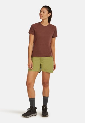 Camisa marrón de manga corta con tela texturizada, combinada con pantalones cortos verdes. Botas de senderismo negras y calcetines grises completan el look outdoor.