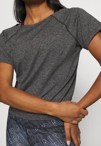 T-paita tumma harmaa urheiluvaatteista, jossa on lyhyet hihat, teksturoitu kangas ja rento istuvuus. Ominaisuuksiin kuuluu pyöreä pääntie ja erottuvat sauman yksityiskohdat.