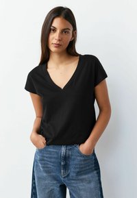 Mustast puuvillast V-kaelusega lühikeste varrukatega t-särk, kombineeritud hele siniste kõrge vöökohaga teksadega; sile tekstuur, vabaaja sobivus.