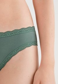 Groene bikini ondergoed met kant, met een gladde textuur, voorzien van een decoratieve scalloped rand en een aansluitend ontwerp.