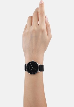 Schwarze analoge Uhr mit rundem Ziffernblatt, silbernen Akzenten, schwarzem Lederarmband und minimalistischen Stundenmarkierungen, die an einem Handgelenk gezeigt wird.