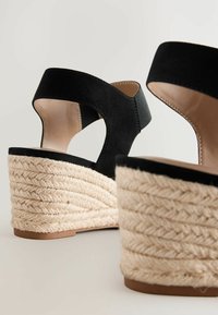 Sandali con tacco a cuneo in suede nero con tacco in juta intrecciata e soletta liscia beige. Presentano una fascia per la caviglia e un design con tagli laterali.