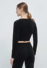 Top corto in velluto nero con maniche lunghe, caratterizzato da un collo rotondo. Abbinato a pantaloni in velluto nero a vita alta. Tessuto liscio.