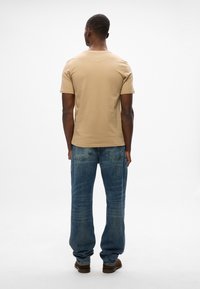 Camiseta de cuello redondo color beige, de manga corta y diseño ajustado. Llevada con vaqueros azules holgados, con piernas estrechas y bolsillos traseros.