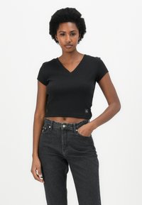 Black cropped t-shirt with short sleeves and a V-neck design. Paired with high-waisted dark gray jeans featuring front pockets.