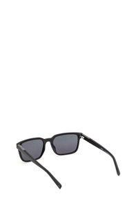 Occhiali da sole neri con lenti rettangolari, finitura opaca, dettagli argentati sulle aste e lenti con gradiente scuro.