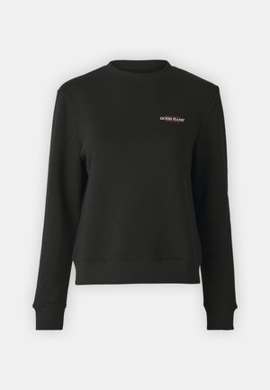 Sweatshirt noir en tissu doux, avec un col rond et des poignets côtelés. L'avant présente un petit logo "GUESS JEANS" en blanc et rouge.