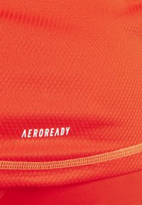 Felorange AEROREADY-stof heeft een textuur met een honingraatpatroon en contrasterende stiksels langs de naad. Zacht en ademend materiaal.