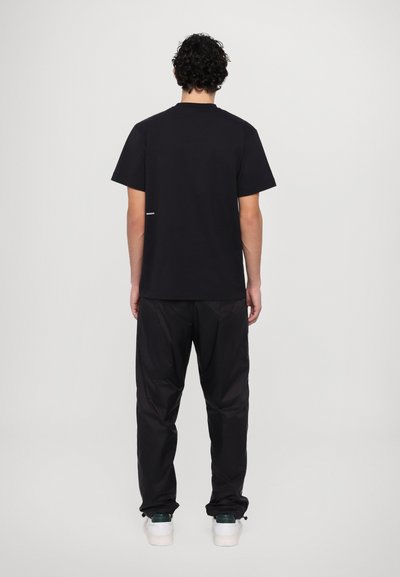 Tricou negru din bumbac, cu mâneci scurte, guler rotund și un mic logo alb în spate, asortat cu pantaloni negri, ușori, cu croi lejer.