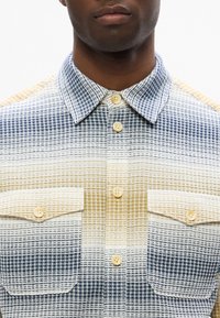 Gewebtes Karoshirt in Creme-, Blau- und hellgoldenen Farbtönen. Mit einem Button-Down-Kragen, vorderem Knopfverschluss und zwei Brusttaschen.